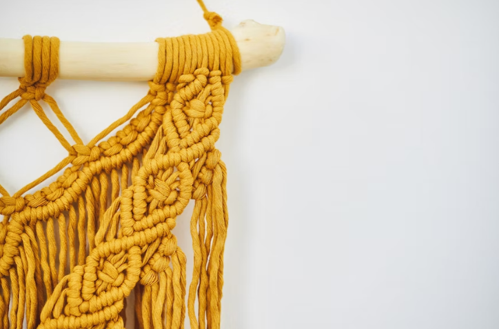 A yellow threaded macramé article hanging on the wall.